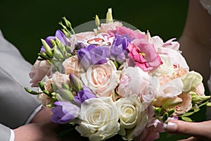 Hands of bride and groom holding wedding bouquet