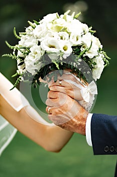 Hands of the bride and groom intertwined and hold a wedding bouquet of delicate white roses, eustomas. Close-up. Hands of the