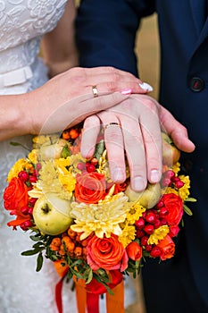 Hands of the bride and groom with rings, folded on a bouquet