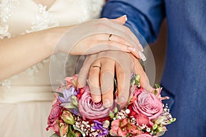 Hands of the bride and groom with rings, folded on a bouquet