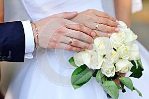 Hands of bride and groom with rings on wedding bouquet