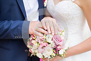Hands of bride and groom with rings on wedding bouquet. Marriage and love concept