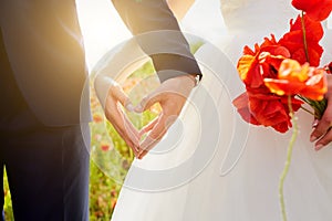 Hands of bride and groom in a shape of heart. Wedding ,love,heartconcept. In the hands of the bride bouquet of poppies. Wedding c