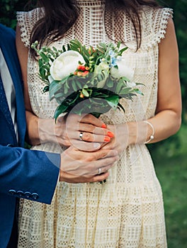 Hands of the bride and groom with wedding rings, bouquet of fresh flowers, vintage lace dress. Concept of marriage, love, family