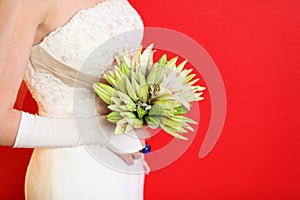 Hands of bride hold bouquet of lilies on red