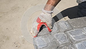 Hands of a builder in his orange gloved hands fitting laying new exterior paving stones carefully placing one in