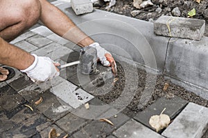 Hands of a builder in his orange gloved hands with a hammer fitting laying new exterior paving stones carefully placing
