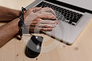 Hands of businessman addicted to work bond with mouse cable to computer laptop in workaholic photo