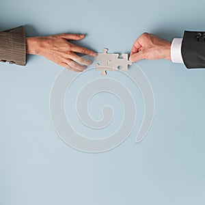 Hands of a businessman and businesswoman joining two blank matching puzzle pieces