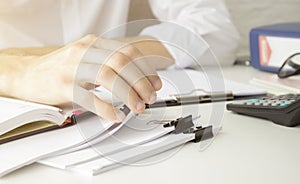 Hands of businessman hold pen for work in stacks of paper files, information search for business reports and heaps o