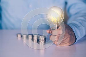 Hands of businessman holding light bulb while coin on desk, saving and finance for success.