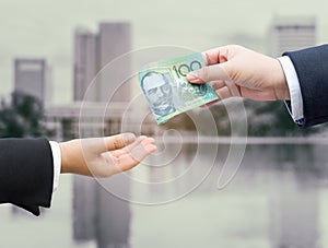 Hands of businessman passing Australian dollar (AUD) banknote.