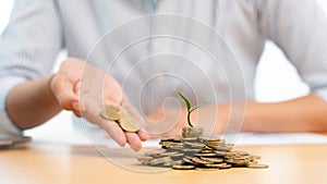 Hands of businessman putting coin into plant sprouting growing up to profit, demonstrating financial growth through saving plans