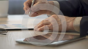 Hands of businessman zooming on tablet, office worker making notes on graph