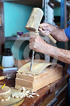 Hands of cabinetmaker carving wood with a chisel and hammer