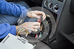 The hands of the car electrician connect the cables from the radio to the car`s electrical system.