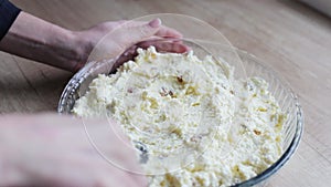 Hands carefully preparing cheese casserole with raisins. Cottage cheese mass for the pie in a transparent baking dish