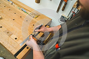 Hands of carpenter carefully drawing line using marker and ruler on wooden plank
