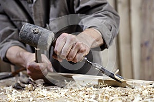 Hands of carpenter with a hammer and chisel on workbench in carpentry