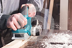 The hands of a carpenter working woodworking power tools. Close up of the work of the electric planer