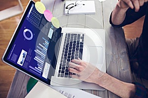 Hands of caucasian businessman sitting at desk, using laptop with statistical data on screen photo