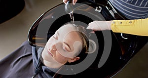 Hands of caucasian female hairdresser washing hair of relaxed female customer at hair salon