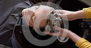 Hands of caucasian female hairdresser washing hair of relaxed female customer at hair salon