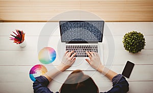 Hands of caucasian female programmer with colour charts using laptop with coding on screen