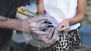 The hands of a caucasian male engraver grind a silver souvenir with a girl.