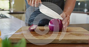Hands of caucasian pregnant woman wearing apron and cutting onion