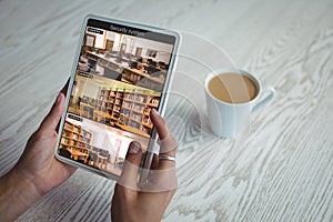 Hands of caucasian woman holding tablet with view of library from security cameras on screen