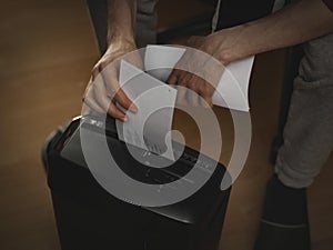 Hands of a caucasian young man destroying documents in a paper cutting machine