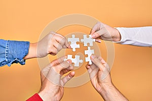 Hands of caucasian young people connecting pieces of puzzle over isolated yellow background