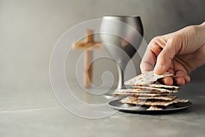 Hands with chalice and communion matzo bread, wooden cross on grey background. Christian communion for reminder of Jesus sacrifice
