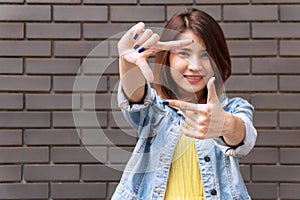 Hands of cheerful woman making frame gesture on brown background with copy space. Focus hands