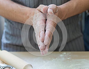 The hands of the chef knead the dough on a wooden table