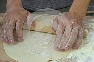 The hands of the chef knead the dough on a wooden table