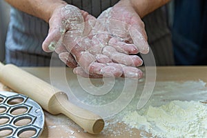 The hands of the chef knead the dough on a wooden table