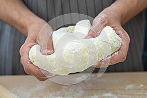 The hands of the chef knead the dough on a wooden table
