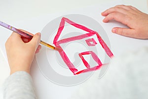 Hands of child drawing red house