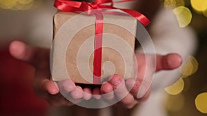 Hands of child holding Christmas gift box closeup. Small present with red ribbon