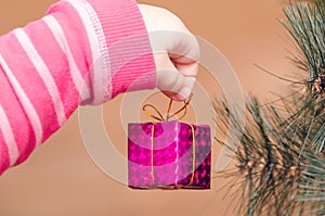 Hands of a child holding a small gift, decoration on a Christmas tree