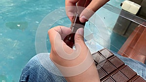 Hands of a child kid breaking a bar of chocolate into pieces and giving one piece to a camera