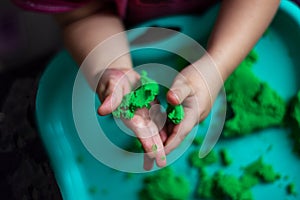 Hands of a child playing with green magic sand. Children`s homework. Little girl is playing with kinetic sand. Kinetic sand in a