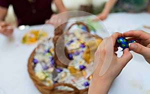 Hands of a child unwrap a chocolate candy egg with a large Easter egg basket in the background during Easter cellebrations