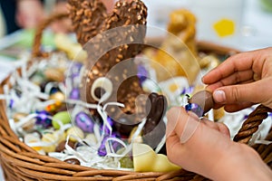 Hands of a child unwrap a chocolate candy egg with a large Easter egg basket in the background during Easter cellebrations