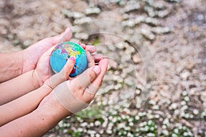 Hands of children daughter and adult mother embrace the blue globes on soiled background and blurred grass and white flowers.