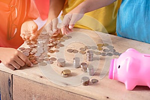 Hands of children are helping putting coins into piggy bank on white background
