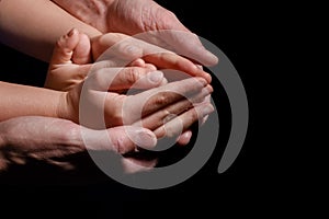 Hands of children and parents holding and supporting each other on a black background