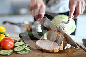 Hands chop ready baked pork meat and vegetables